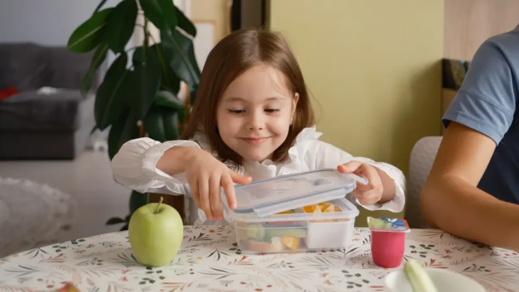 young girl carefully packs a healthy lunch box for school, filled with fresh fruits, vegetables, and nutritious snacks.